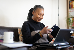 Healthy woman living with HIV working from her home living room on a laptop and using her smartphone